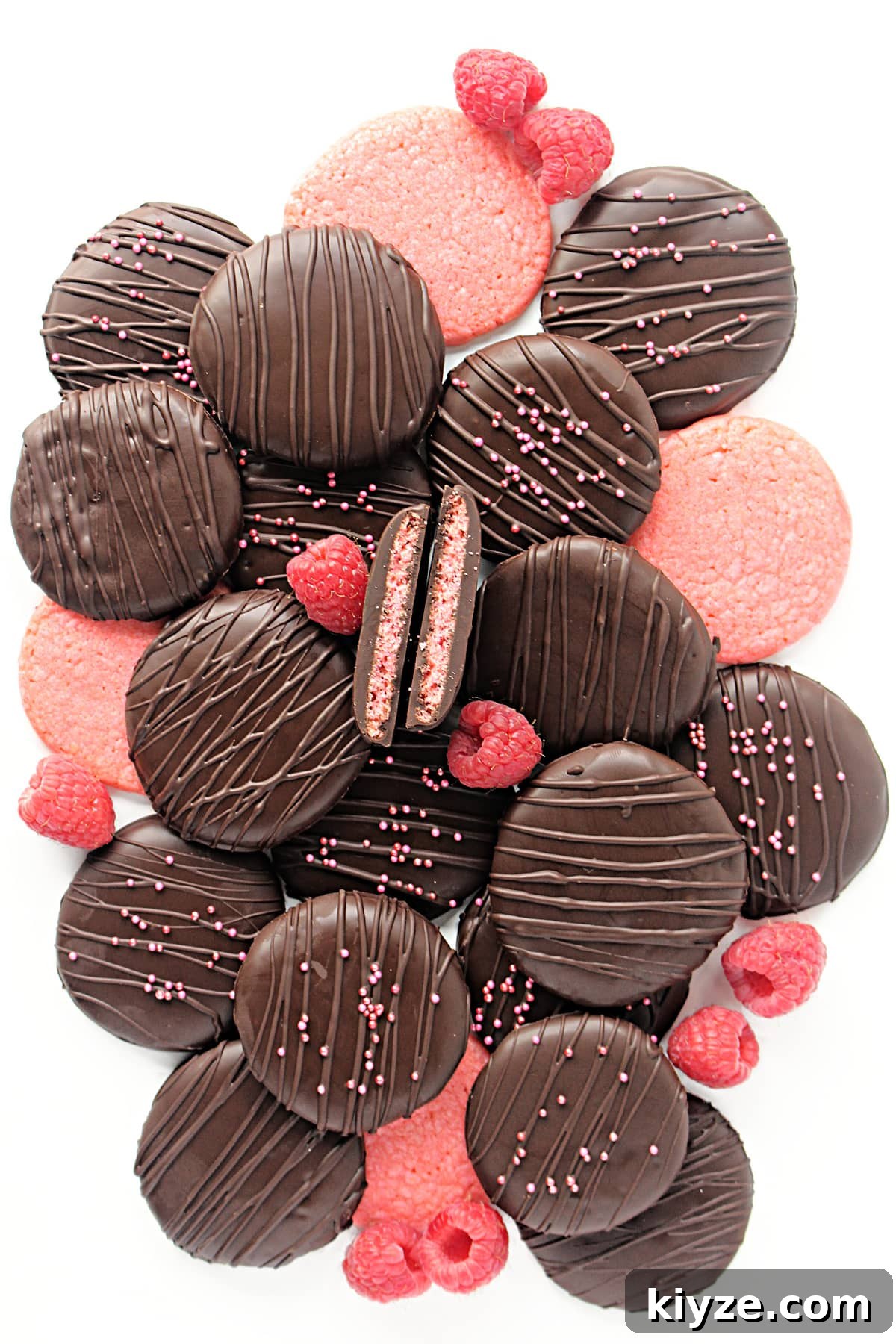 Raspberry Rally Cookies Recipe — Soft Homemade Jam-Filled Cookies 2 Thin, pink raspberry cookies coated in chocolate decorated with chocolate zigzags and sprinkles.