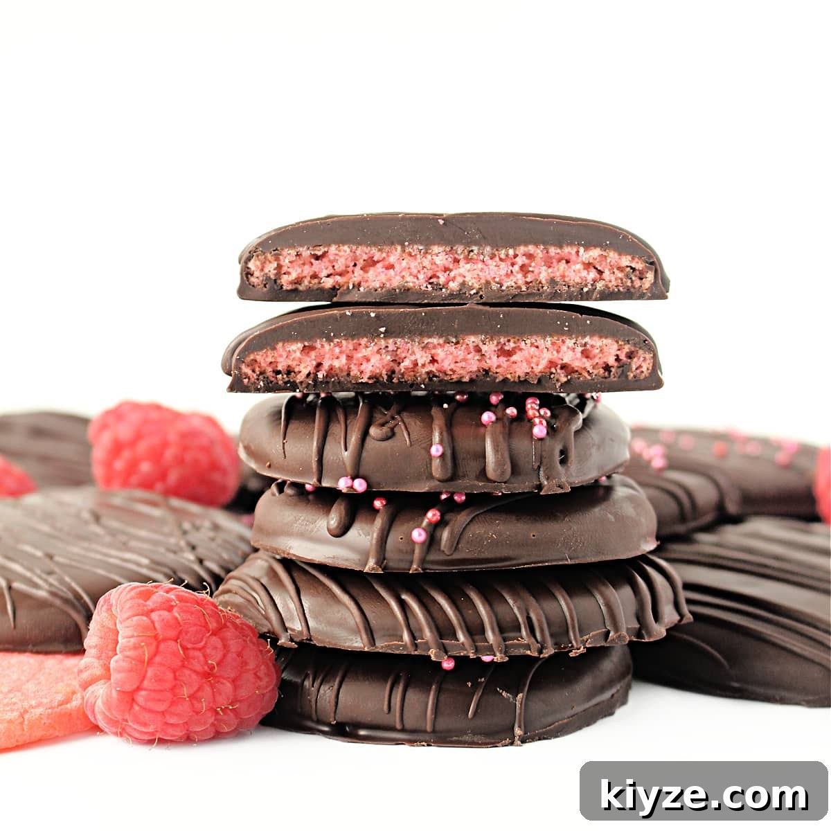 Raspberry Rally Cookies Recipe — Soft Homemade Jam-Filled Cookies 6 Stack of chocolate coated cookies with two cookie halves on top showing pink cookie inside.