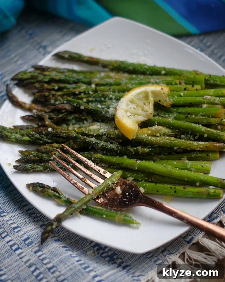 Roasted Lemon Asparagus on a white plate with a slice of lemon and parmesan cheese.