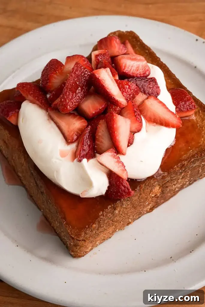 honey butter toast topped with rose whipped cream and strawberries on a plate