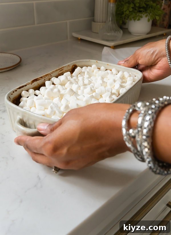 A woman holding a pan of sweet potato casserole topped with marshmallow fluff and mini marshmallows.