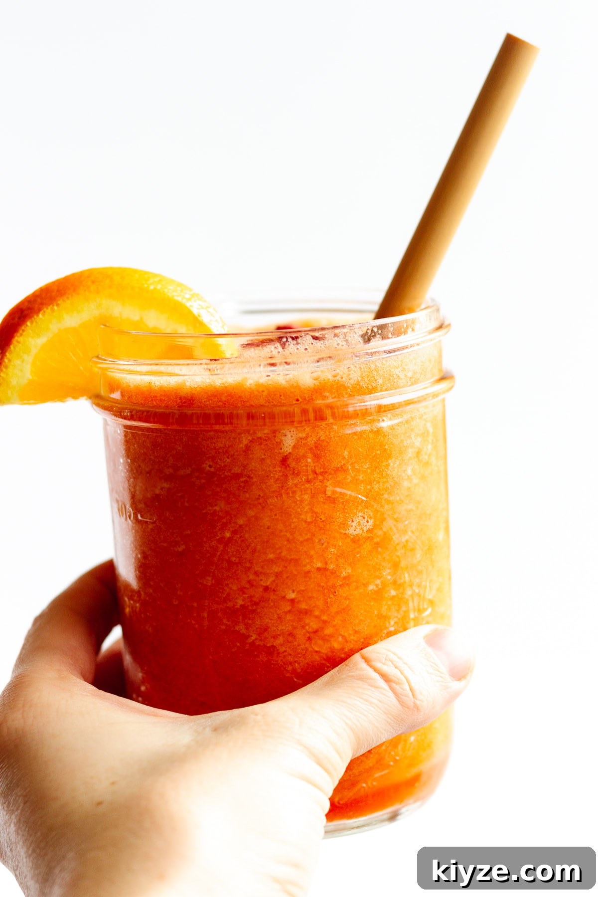 High-Vitamin C Immunity-Boost Smoothie Recipe 2 Hand holding mason jar filled with Vitamin C Smoothie with an orange slice on the edge and bamboo straw.