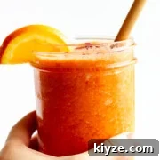 Hand holding a vitamin c powerhouse smoothie in a glass jar with bamboo straw and orange slice garnish.