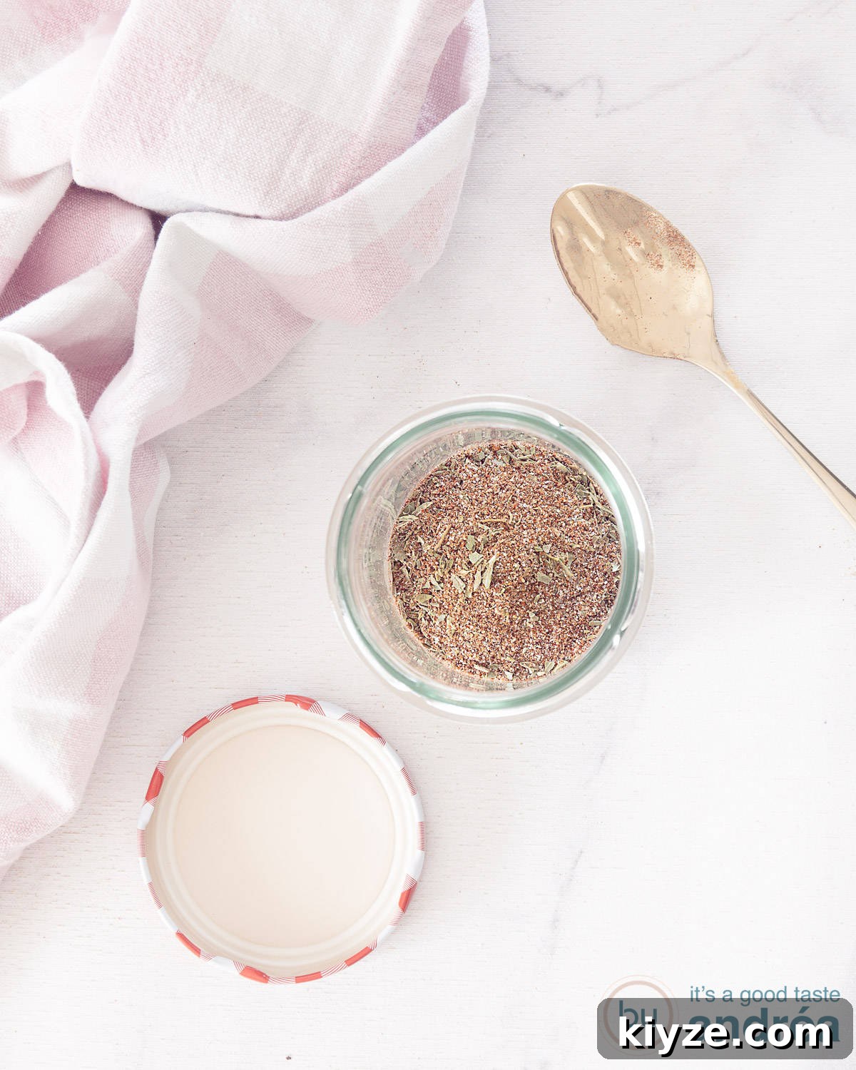 Homemade Chicken Seasoning Mix: Flavorful DIY Blend for Any Dish 3 A photo from above showing a glass jar with homemade chicken seasoning. A white marble surface. A pink and white tea towel at the top left