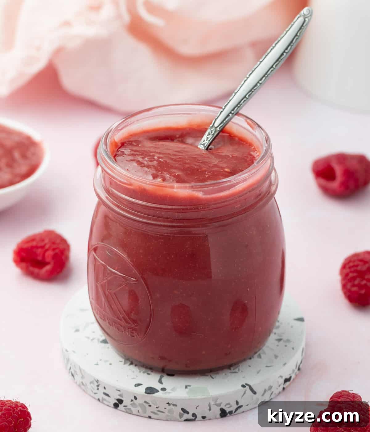 Curd inside a glass jar with a silver spoon on a pink background.