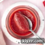 Picking up some raspberry curd from a jar with a spoon seen from above.
