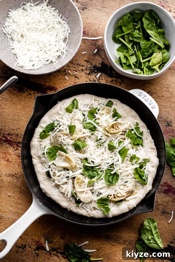 Deep-Dish Spinach and Artichoke Pizza Recipe 5 The unbaked, assembled pizza in a cast iron pan on a wood surface.