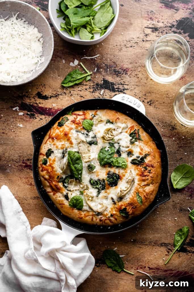 Deep-Dish Spinach and Artichoke Pizza Recipe 6 Baked spinach artichoke pizza in a cast iron skillet on a wooden surface.