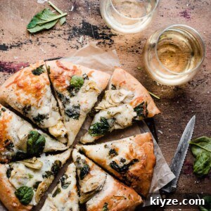 Deep-Dish Spinach and Artichoke Pizza Recipe 8 The sliced spinach artichoke pizza on a wooden backdrop.