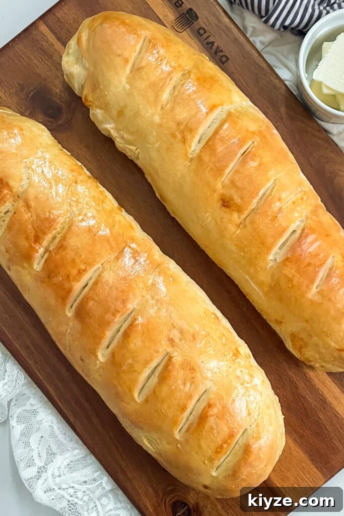 90-Minute Artisan French Bread Recipe for Crisp Crust and Soft Crumb 3 Two loaves of baked French bread on a brown cutting board with a small white jar with sliced butter