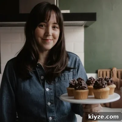Mascarpone Whipped Cream Frosting Recipe — 5 Ingredients 14 Ella from Alpine Ella is holding a cake stand with cupcakes on it.