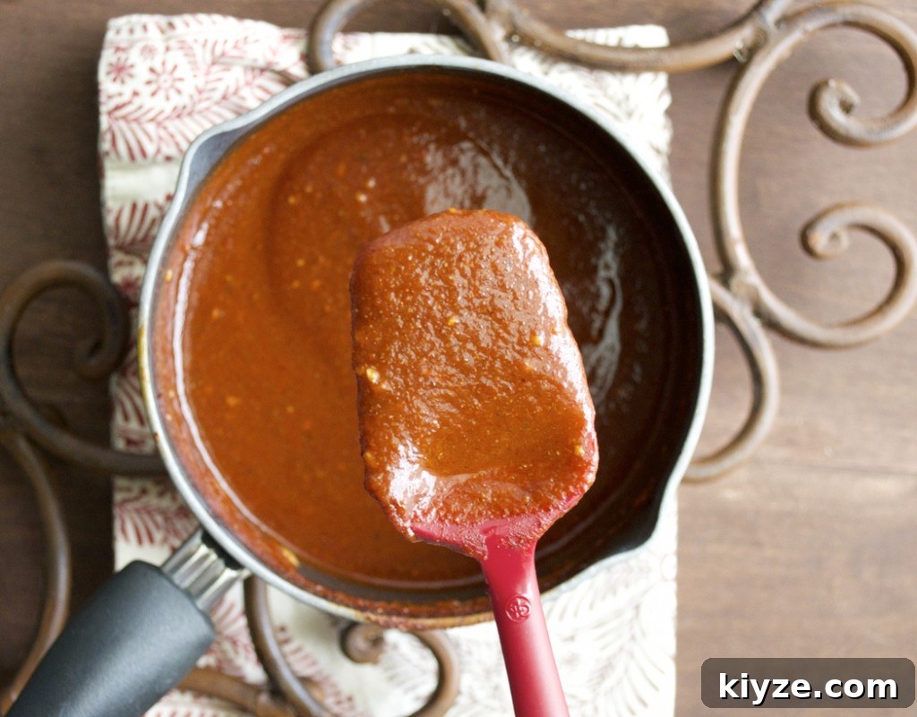 Authentic Homemade Enchilada Sauce Recipe for Rich Flavor 3 homemade red enchilada sauce in a saucepan with a spatula hovering over top
