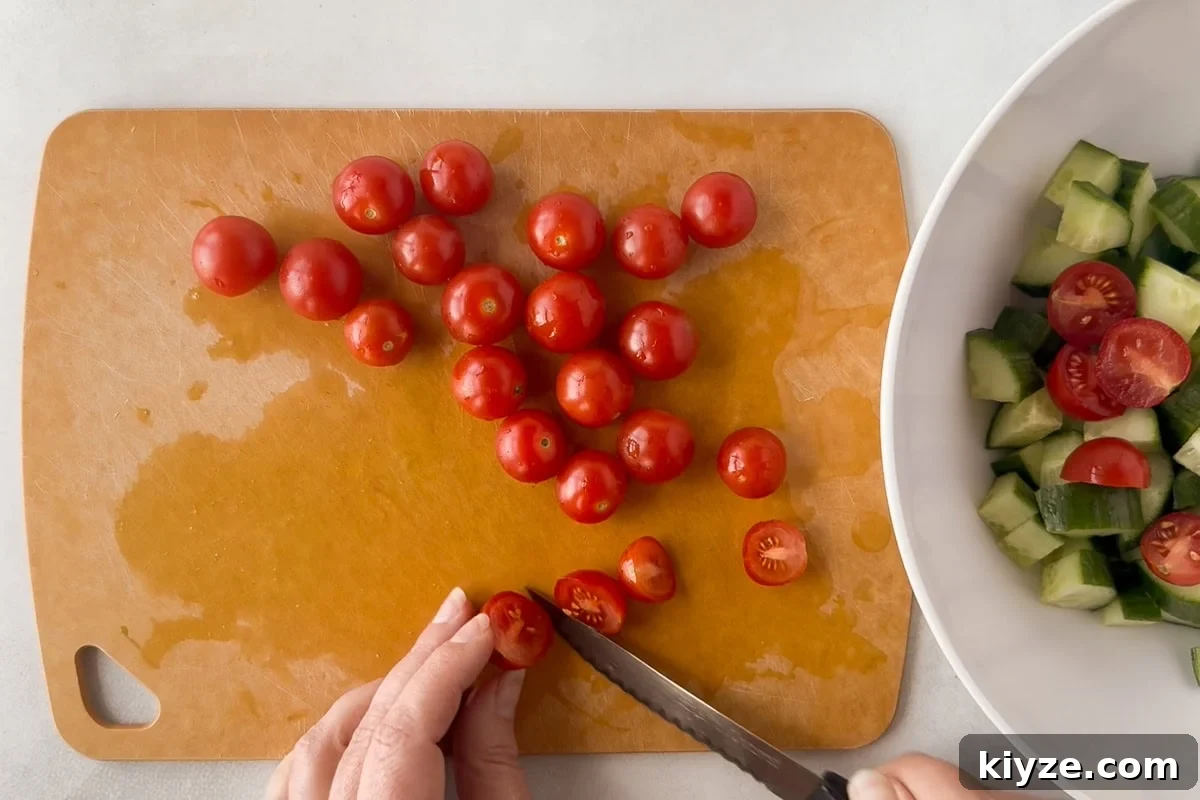 Quick Cucumber Tomato Salad with Feta in 10 Minutes 5 A person uses a knife to slice cherry tomatoes on a brown cutting board. Some tomatoes are whole, while others are halved.