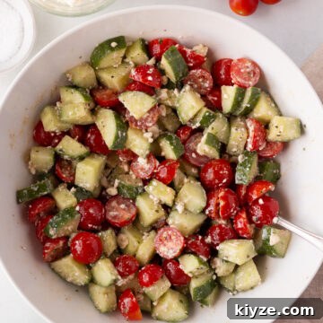 Quick Cucumber Tomato Salad with Feta in 10 Minutes 9 A large white bowl filled with a salad made of chopped cucumbers, halved cherry tomatoes, and crumbled feta cheese; a spoon rests inside the bowl.