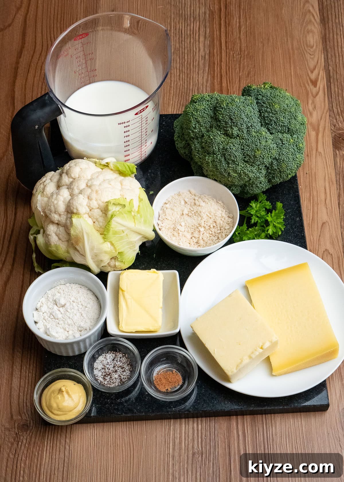 Cheesy Cauliflower and Broccoli Casserole Recipe 17 A jug of whole milk,one broccoli,one cauliflower, panko breadcrumbs, butter, flour, gouda, mature cheddar cheese, salt,pepper, Dijon mustard and and nutmeg in dishes all on a marble chopping board