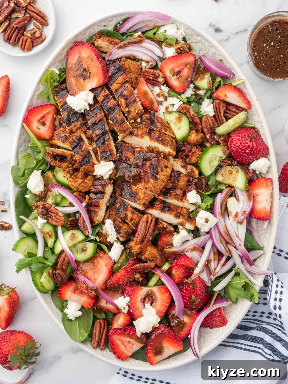 Grilled Chicken and Strawberry Salad with Balsamic Glaze 6 Grilled chicken on spinach salad with fresh strawberries on a serving platter with balsamic dressing and pecans to the side.