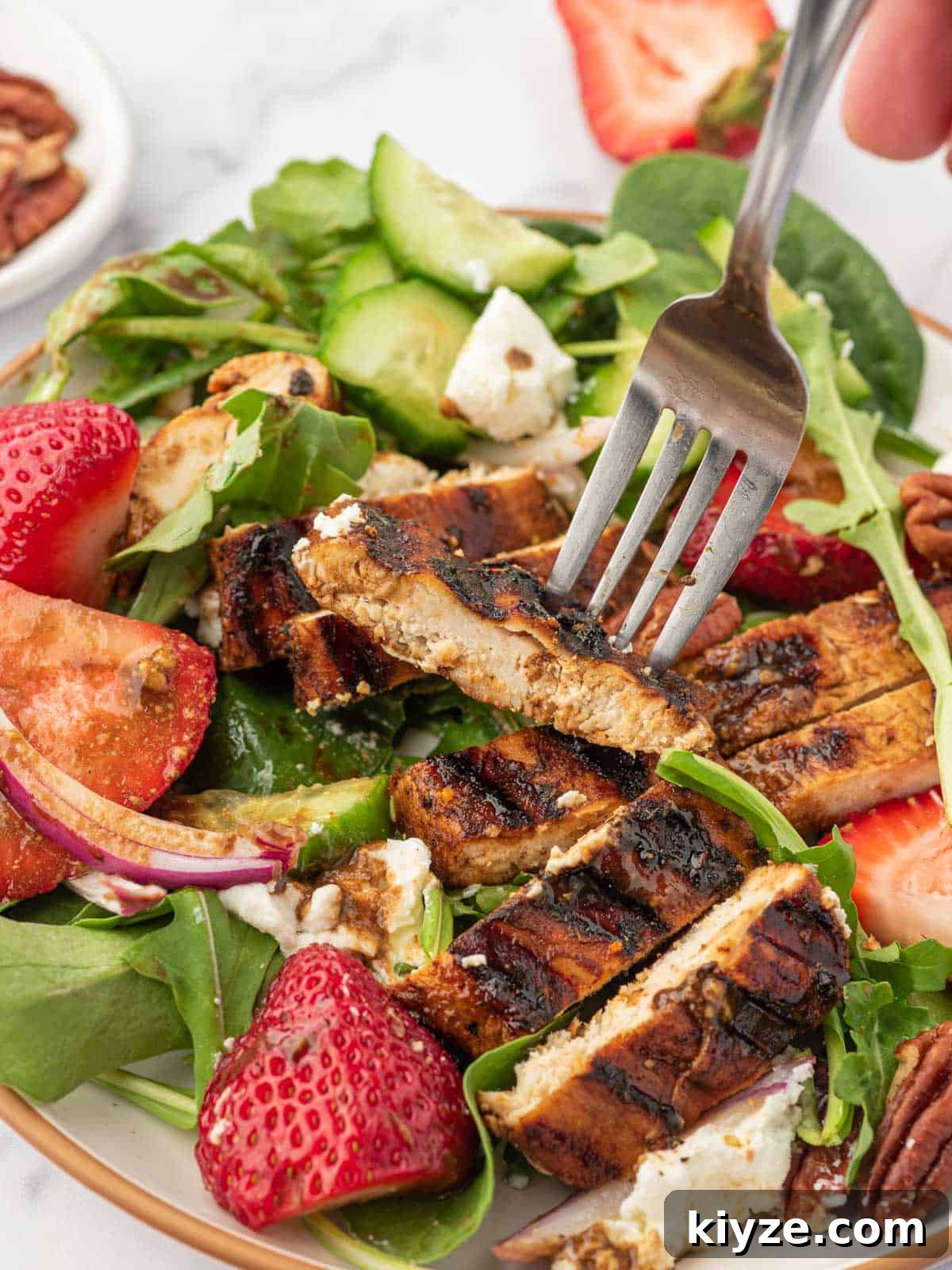 Grilled Chicken and Strawberry Salad with Balsamic Glaze 8 Balsamic grilled chicken on a fork over a plate of spinach and strawberry salad.