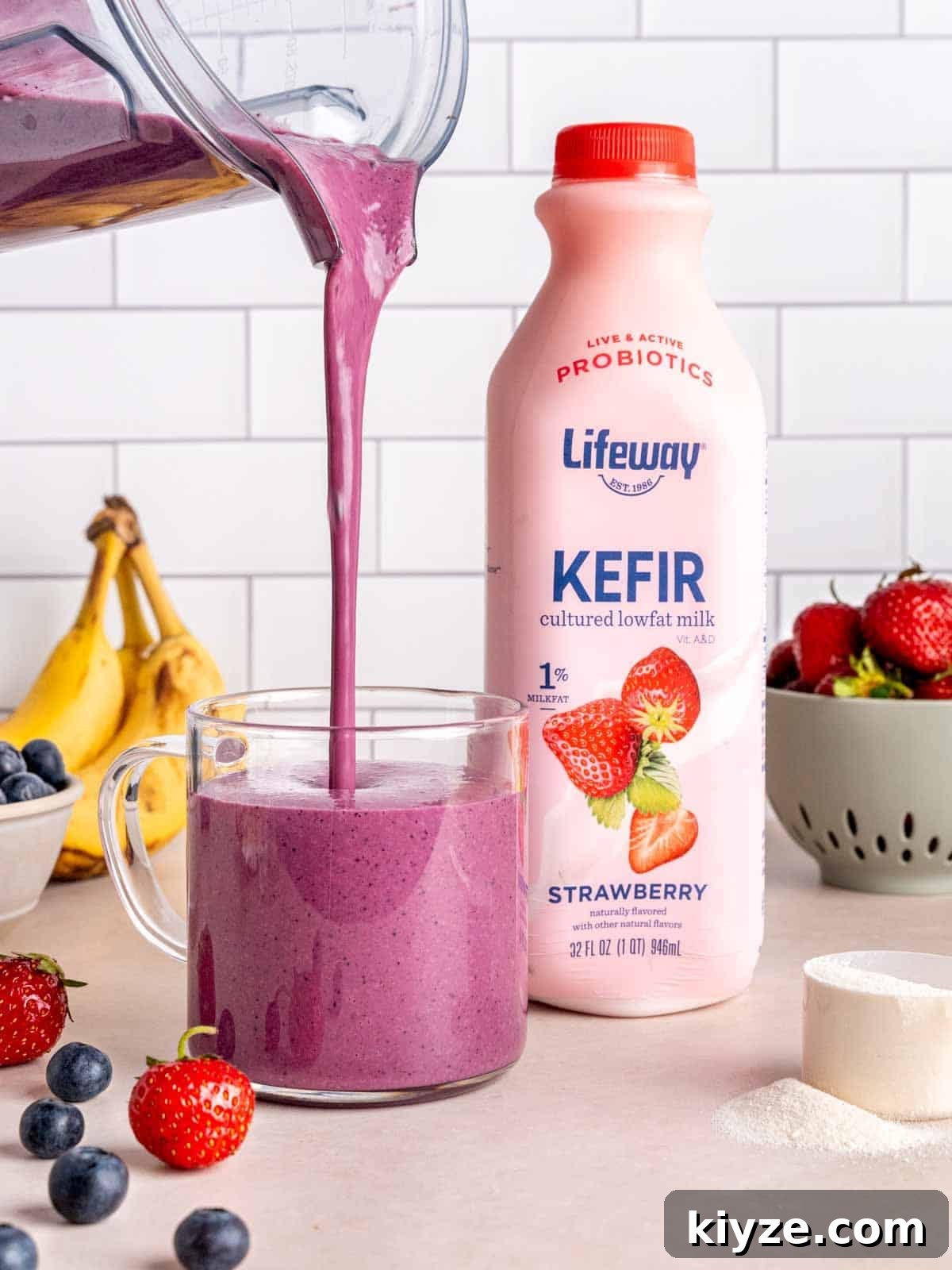 Creamy Banana and Berry Protein Smoothie Recipe 7 Pouring a fruit smoothie into a glass cup next to a bottle of Lifeway Strawberry Kefir.