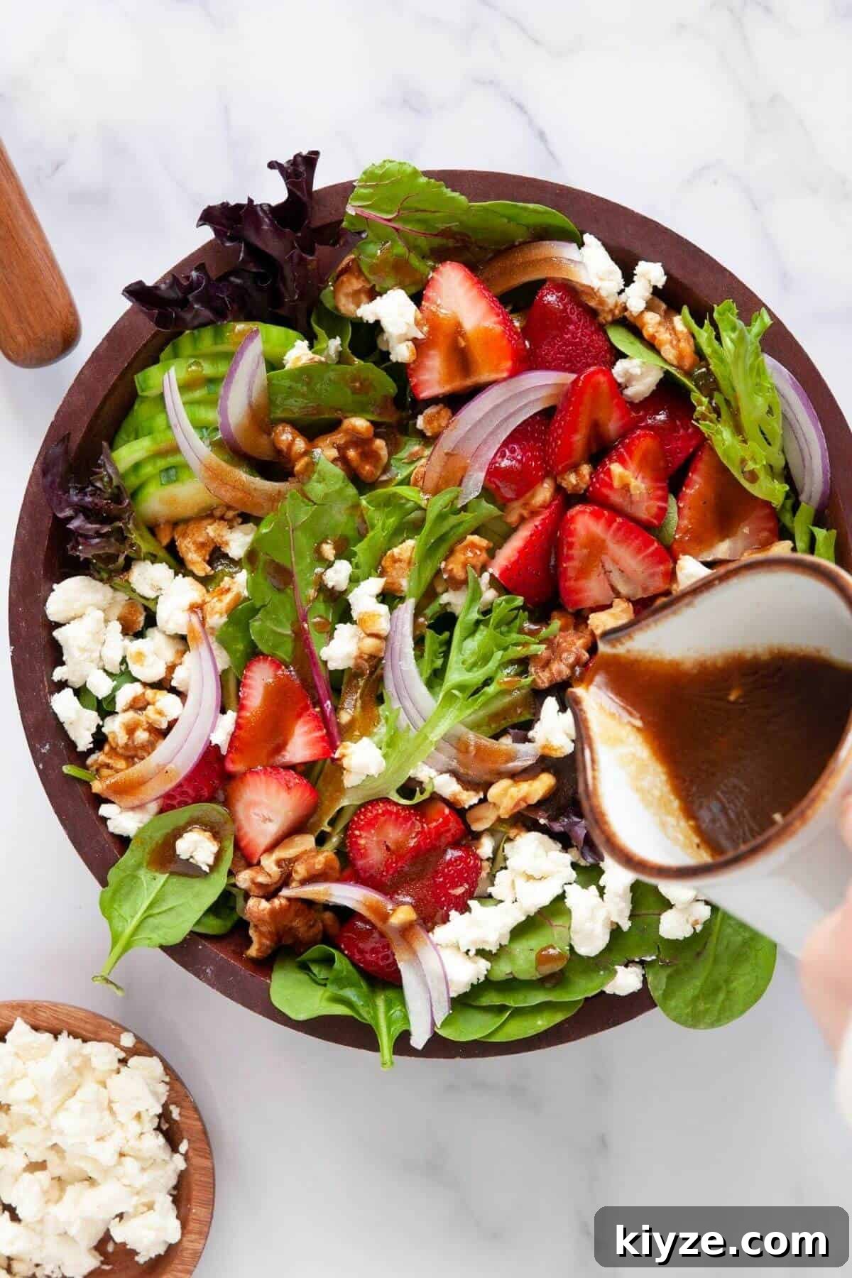 Pouring healthy balsamic vinaigrette on strawberry goat cheese salad with walnuts and cucumbers.