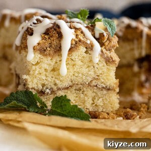 Slice of coffee cake with icing drizzled on top. Mint in the corner for garnish.