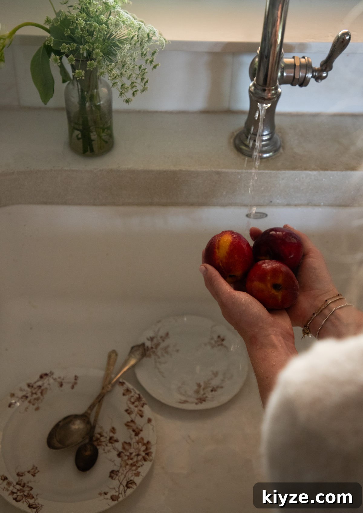 Homemade Peach Cake with Fresh Peach Glaze 2 woman's hands holding 3 peaches above a sink with brown floral dishes in the sink below