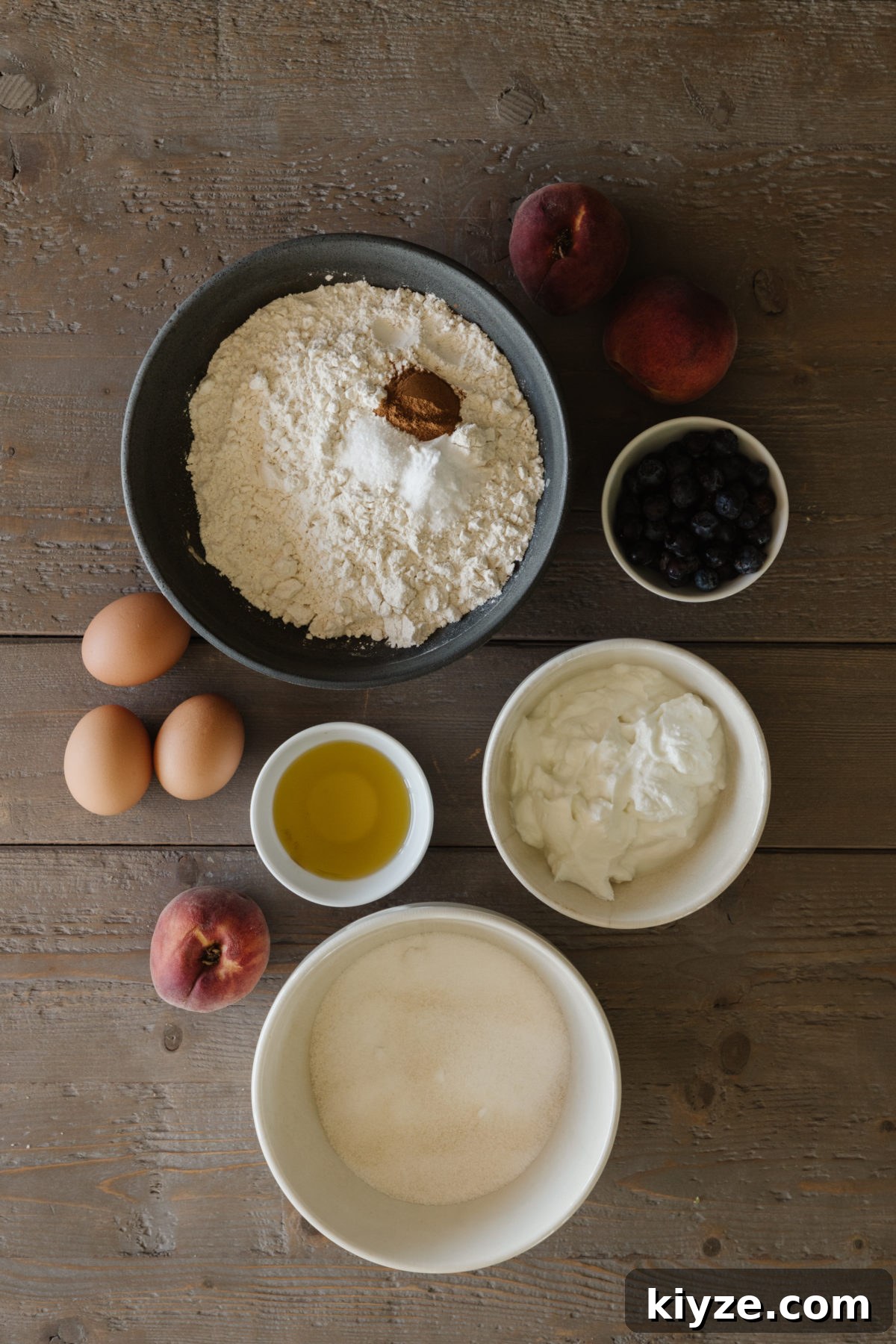 Homemade Peach Cake with Fresh Peach Glaze 4 peach cake ingredients in various neutral colored bowls with eggs and peaches on a rustic wooden table