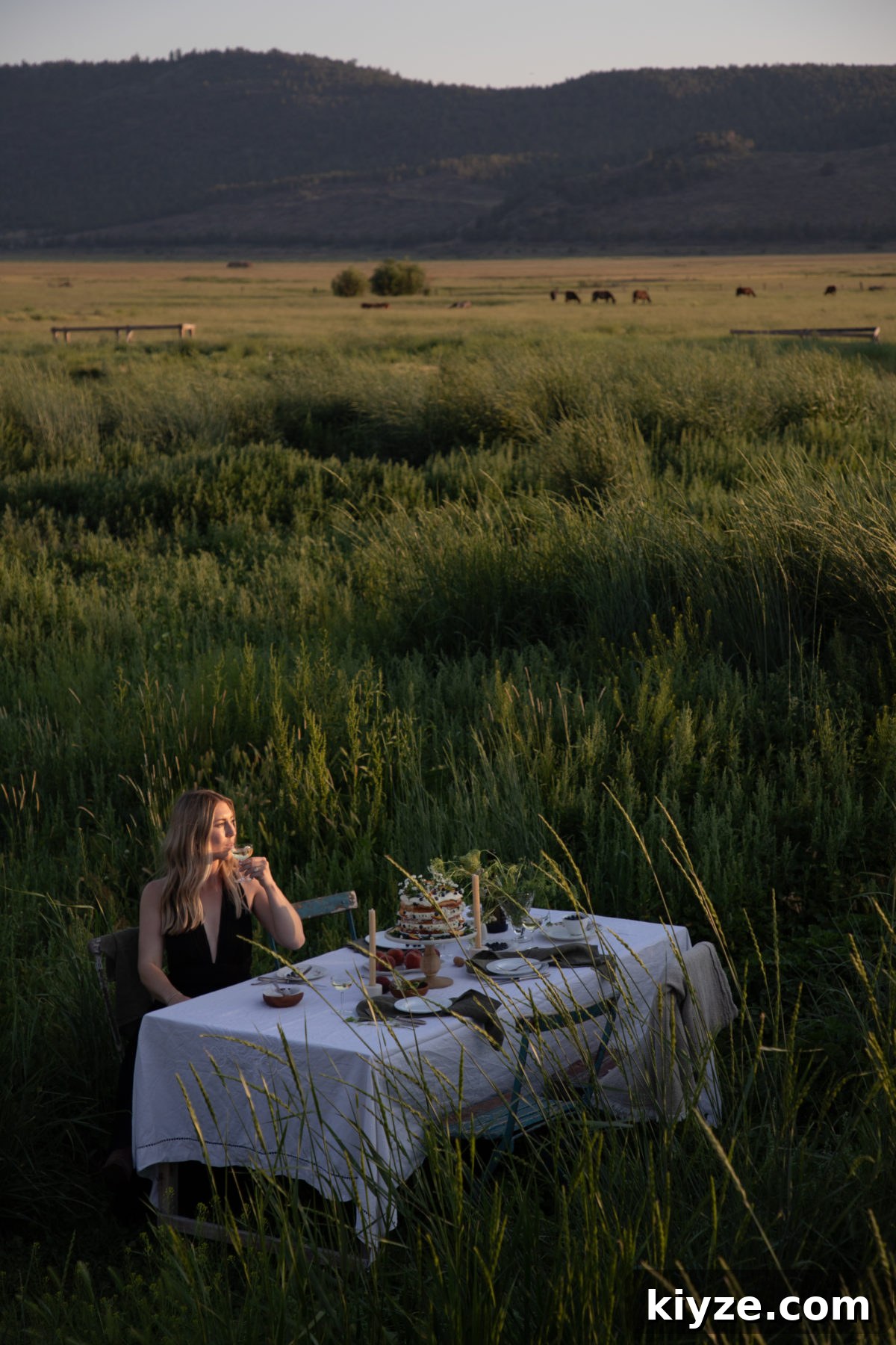 Homemade Peach Cake with Fresh Peach Glaze 6 a woman sitting at a white cloth covered table in the middle of a field with a cake and drinks on the table