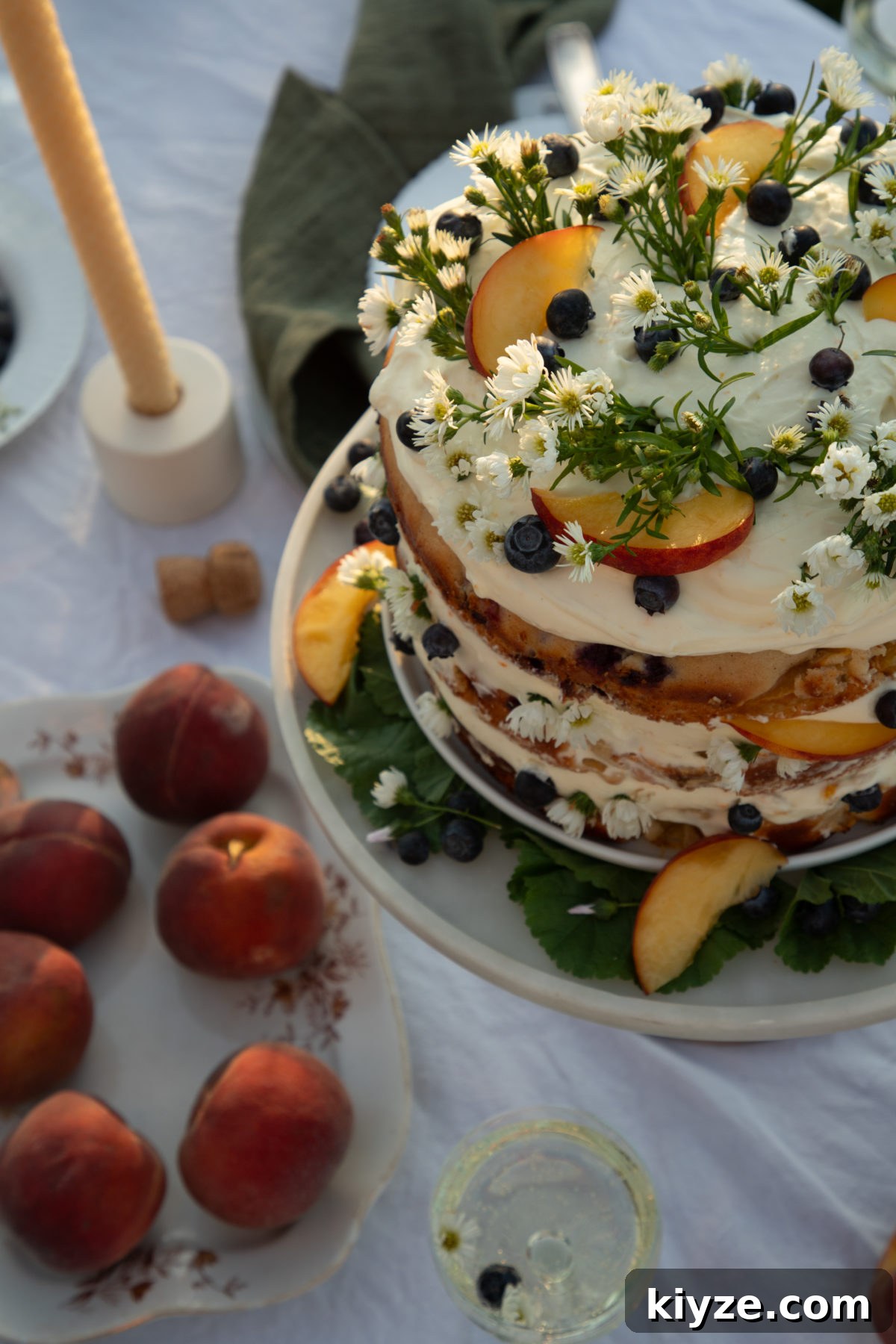 Homemade Peach Cake with Fresh Peach Glaze 7 close-up of peach cake with whipped cream cheese frosting topped with peach slices, blueberries, and camomile flowers