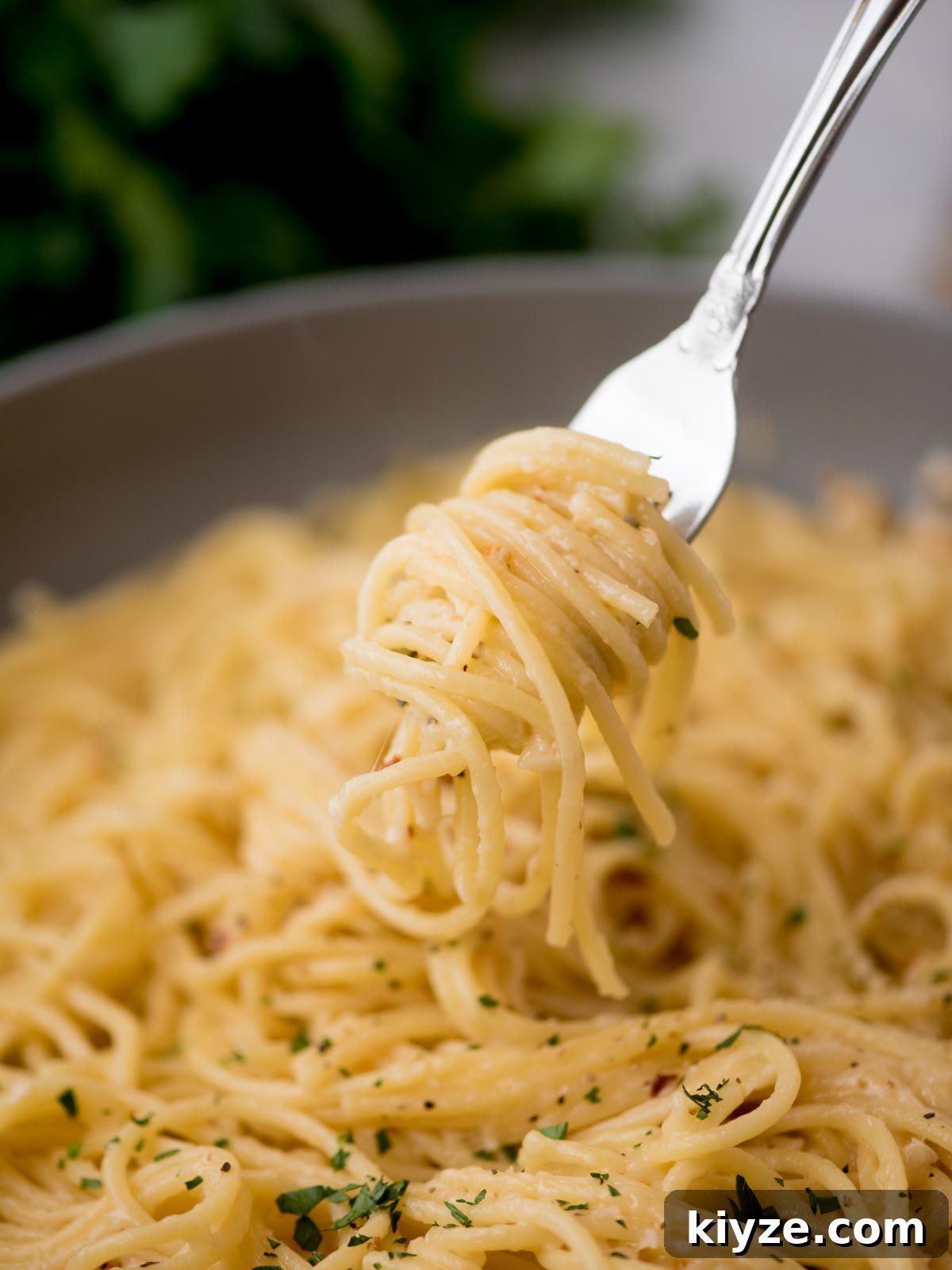Creamy Lemon Garlic Pasta Recipe with Parmesan and Herbs 5 A fork twirls a portion of creamy spaghetti over a bowl. The pasta is topped with finely chopped herbs, giving it a fresh, appetizing look. The background is slightly blurred, focusing on the pastas texture.