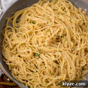 Creamy Lemon Garlic Pasta Recipe with Parmesan and Herbs 6 A skillet filled with spaghetti pasta tossed in a creamy, lemon garlic cheese sauce, topped with freshly ground black pepper and garnished with chopped parsley.