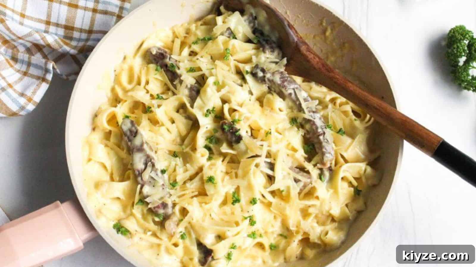 Alfredo steak pasta in skillet with wooden spoon.