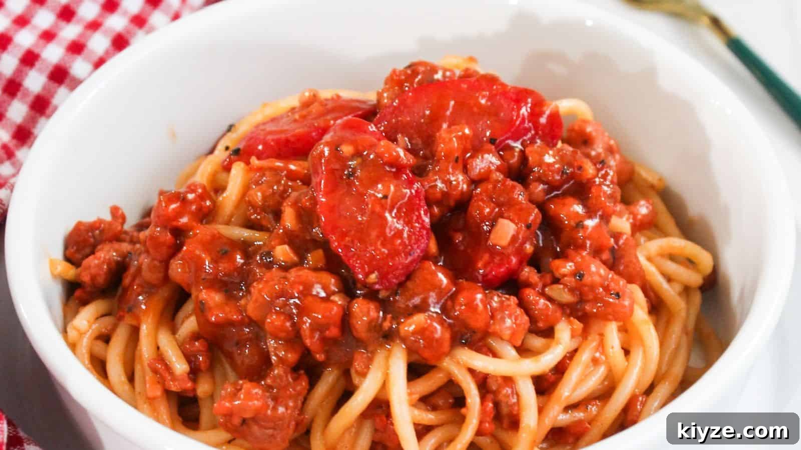 25 Comforting Main Dishes That Make You Forget the Grill 24 A bowl of spaghetti topped with a rich meat sauce placed on a red and white checkered tablecloth.