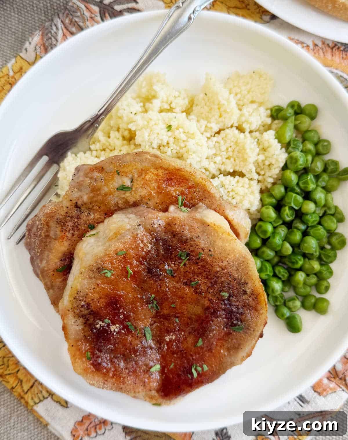 Brown Sugar Baked Pork Chops with Caramelized Glaze 2 brown sugar baked pork chops with couscous and peas on a white plate.