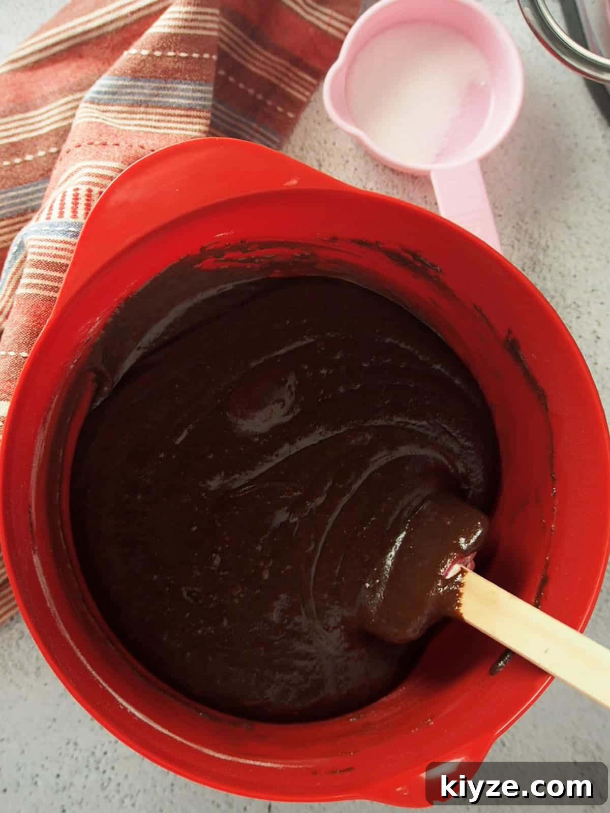 Black Forest Roll Cake Recipe – Chocolate Cherry Swiss Roll 3 melted chocolate and cocoa powder in a red bowl with a spatula.
