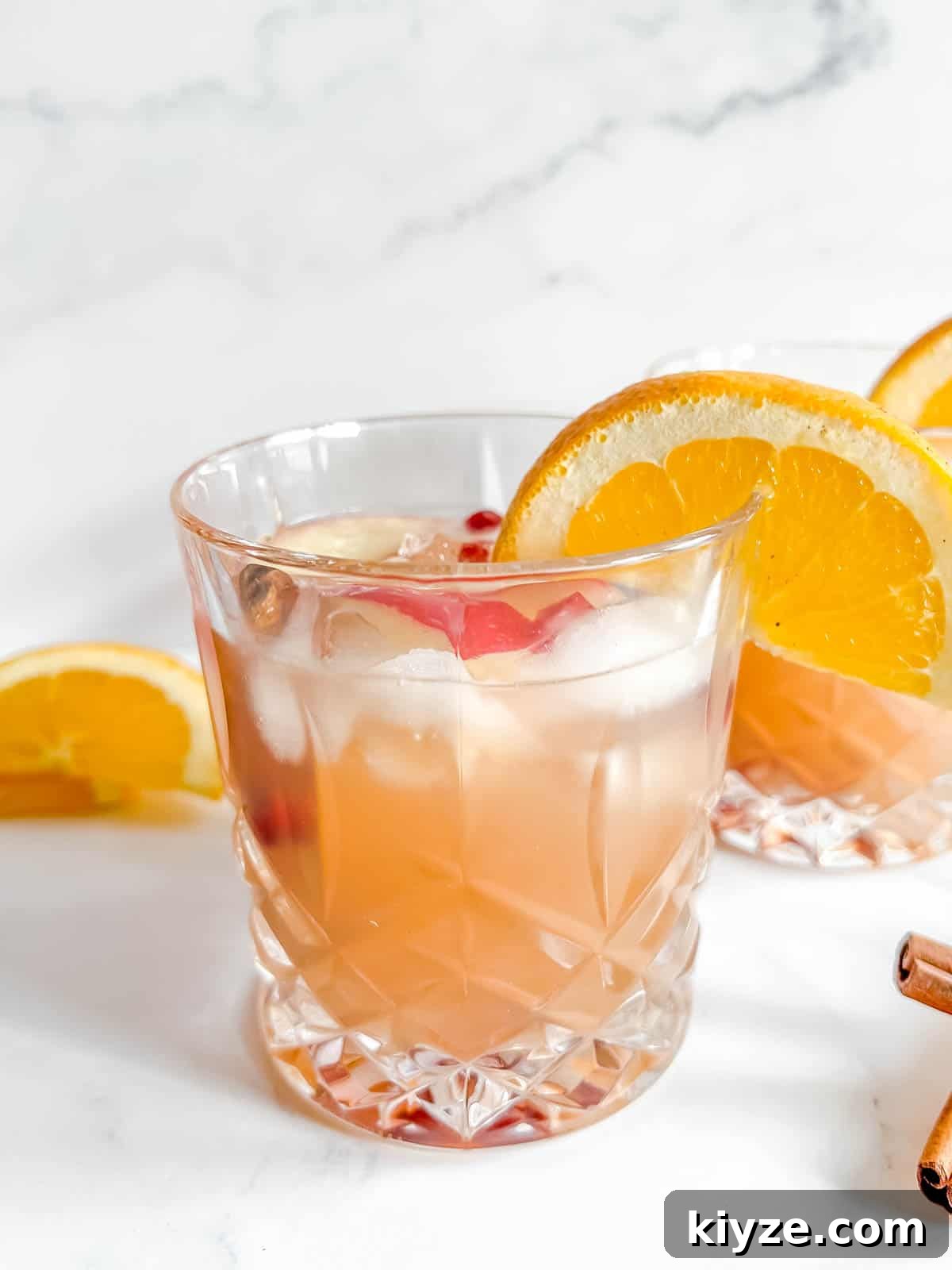 Apple Cider Cocktail in two cups with orange slices on the cups.