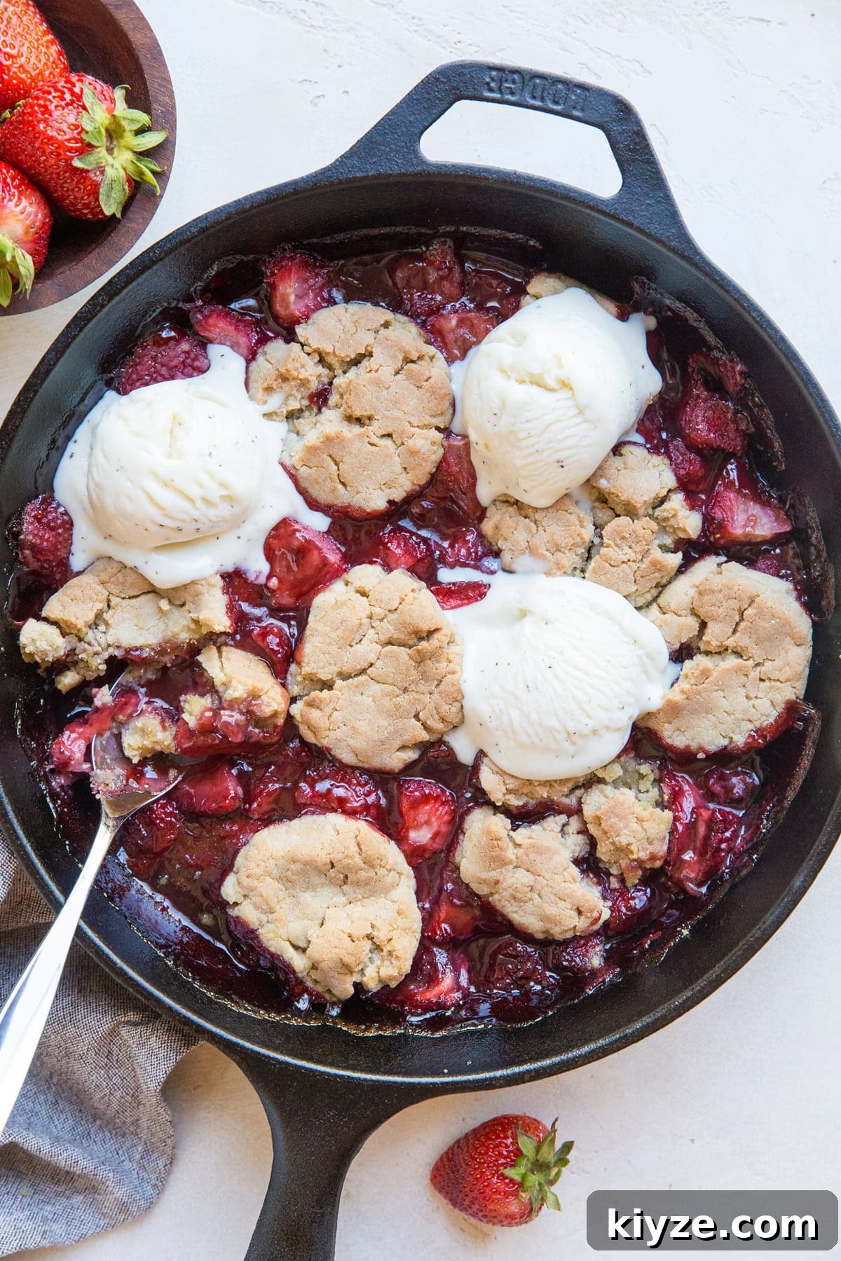 Vegan Gluten-Free Strawberry Cobbler Recipe for Summer Baking 3 Cast iron skillet full of strawberry cobbler with scoops of vanilla ice cream on top and fresh strawberries to the side.