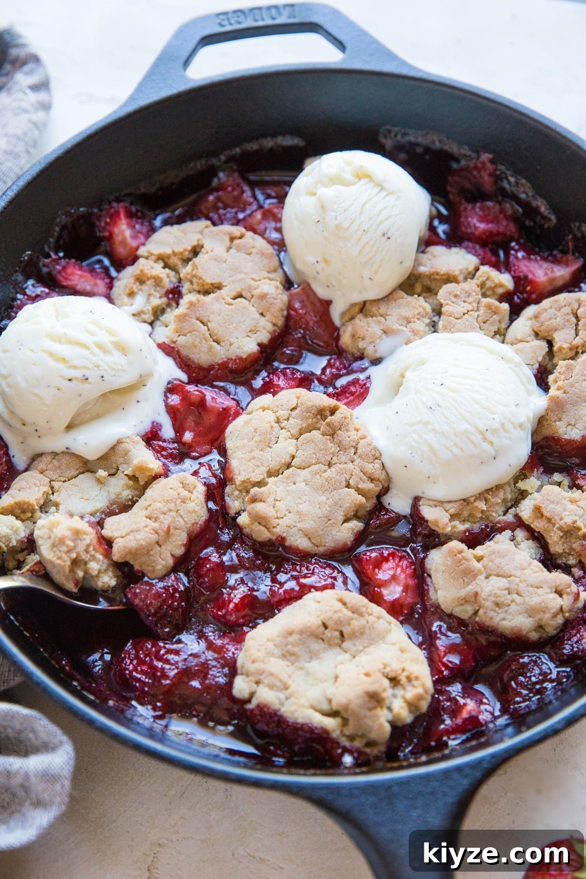 Vegan Gluten-Free Strawberry Cobbler Recipe for Summer Baking 4 Cast iron skillet full of strawberry cobbler with a scoop of ice cream and a serving spoon, ready to serve.
