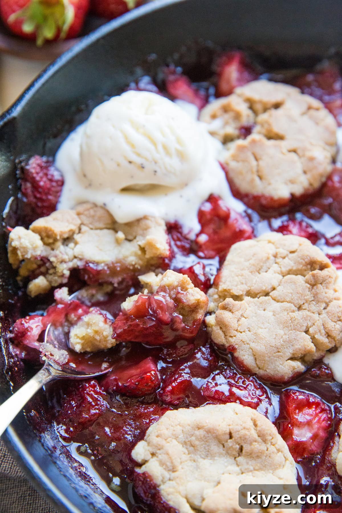 Vegan Gluten-Free Strawberry Cobbler Recipe for Summer Baking 7 Large skillet full of strawberry cobbler with a scoop of melted vanilla ice cream and a spoon scooping out some of the cobbler.