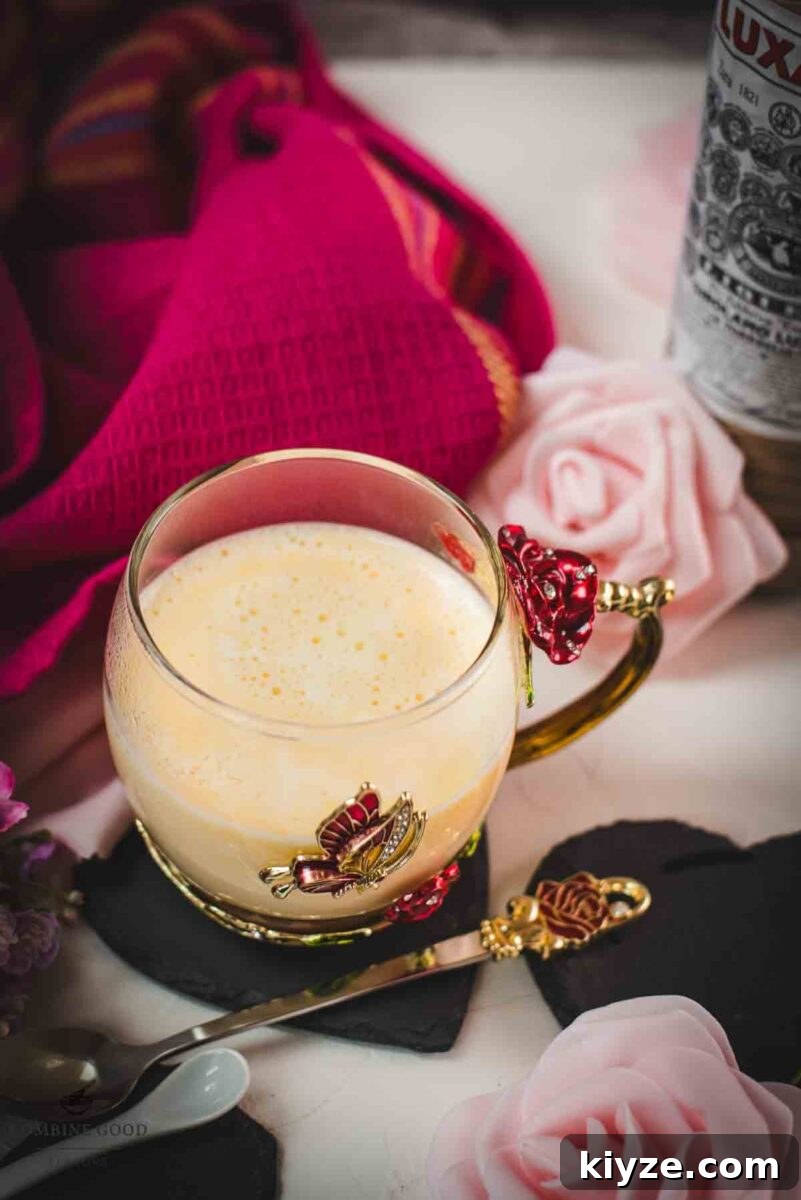 Classic Maraschino Milk Cocktail Recipe for Vintage Flavor 2 Creamy, dreamy Maraschino liqueur cocktail served in whimsical cup with red and golden butterflies and flowers. Placed on a black slate heart shaped coaster.