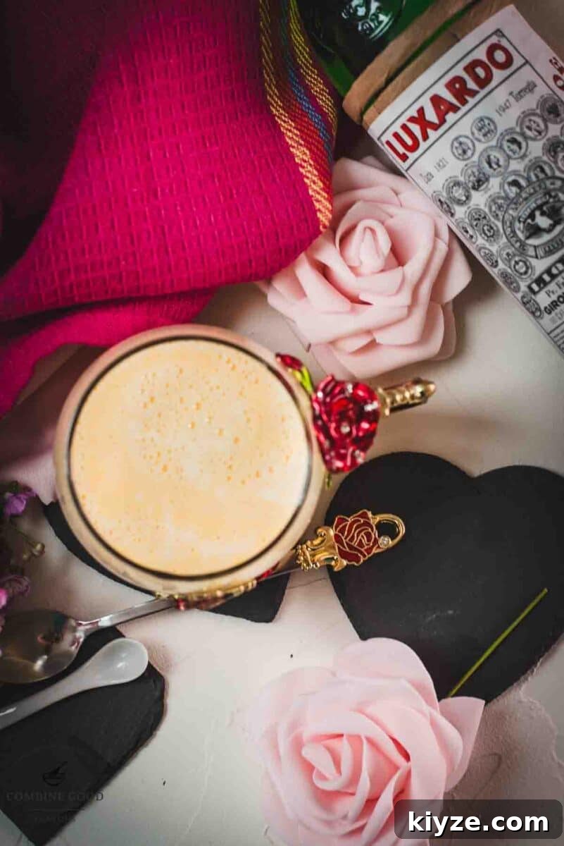 Classic Maraschino Milk Cocktail Recipe for Vintage Flavor 10 Creamy, dreamy Maraschino liqueur cocktail served in whimsical cup with red and golden butterflies and flowers. Placed on a black slate heart shaped coaster.