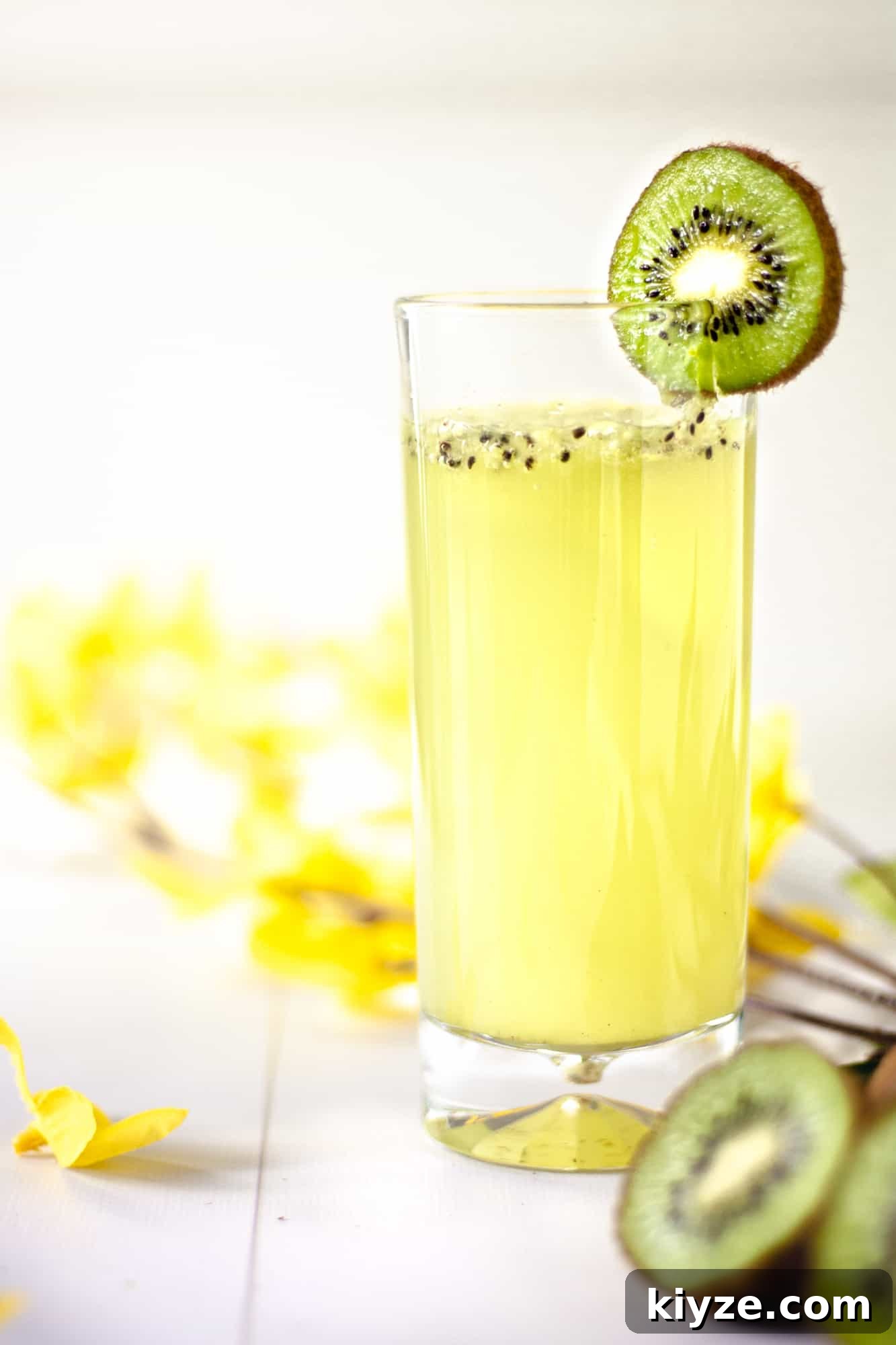 Refreshing Kiwi Gin Cocktail Recipe for Summer Sips 5 Up close view of a glass of kiwi gin cocktail garnished with kiwi, and kiwis and yellow flowers in the background
