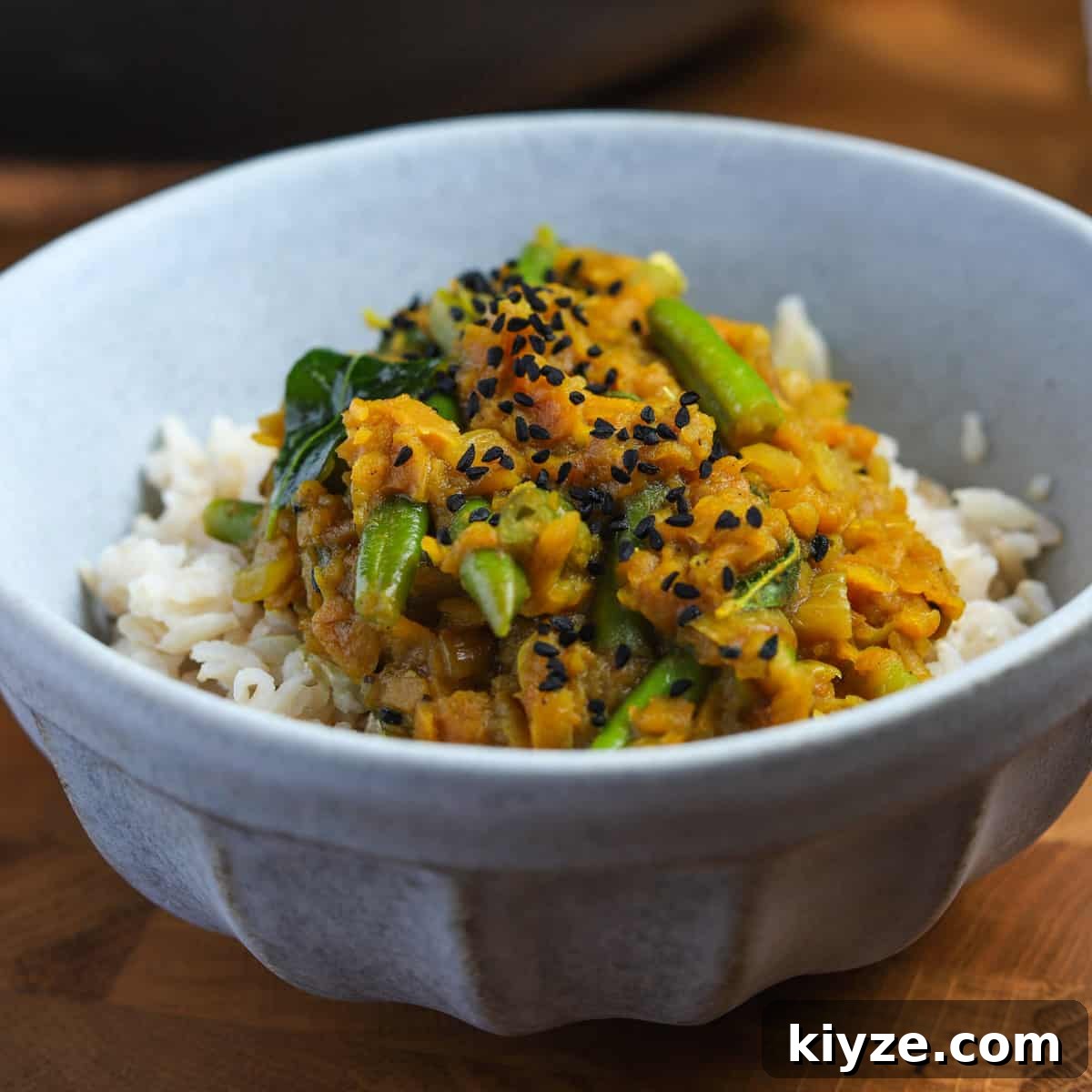 North Indian Pumpkin and Green Bean Curry (Vegan) 2 Photo of a blue bowl filled with pumpkin curry on a mound of brown rice, all on a wooden tabletop.