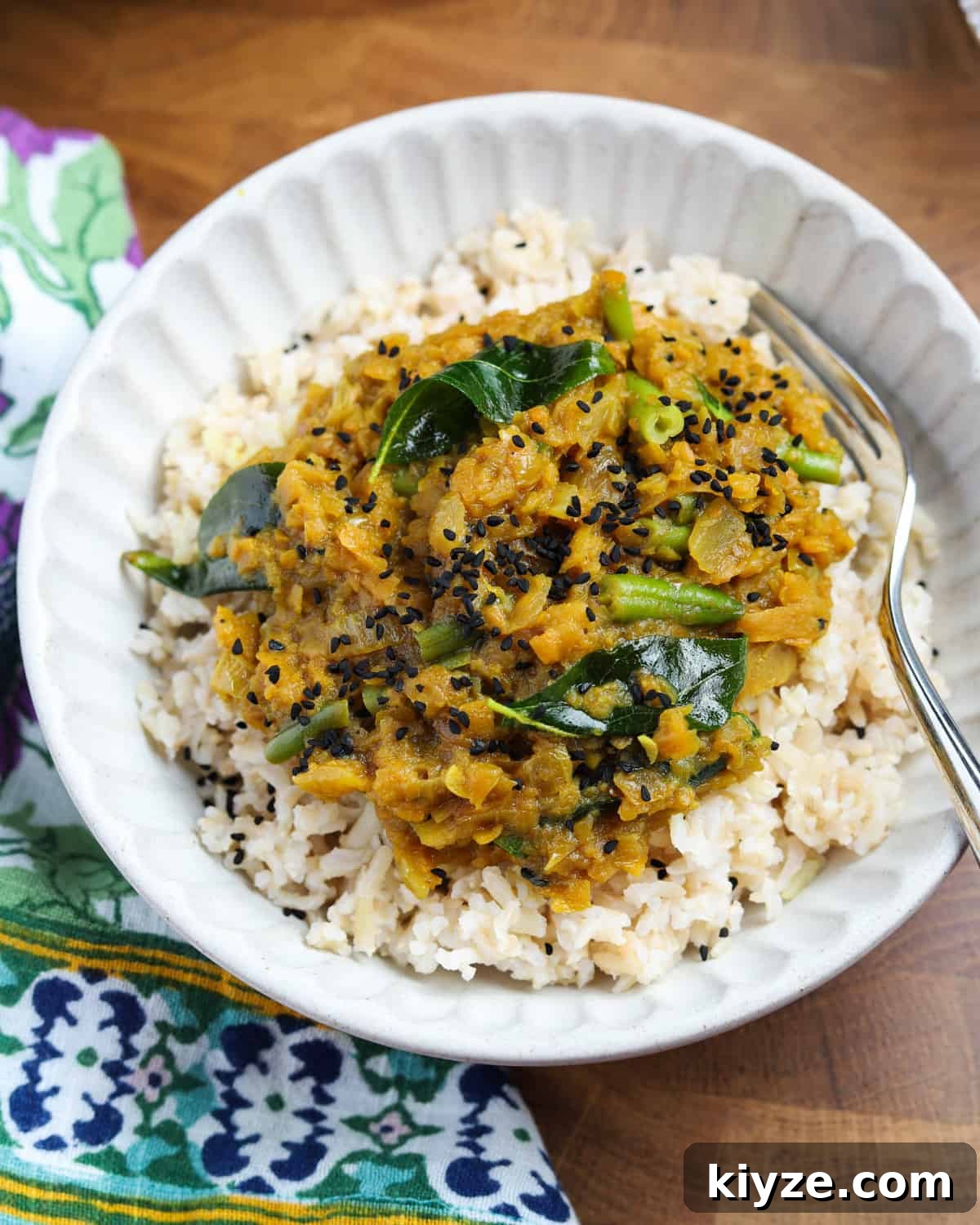 North Indian Pumpkin and Green Bean Curry (Vegan) 5 overhead photo of pumpkin curry served over rice in a white bowl on a wooden table with a napkin tucked underneath.