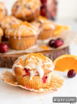 cranberry orange muffin with glaze and orange zest on open paper muffin liner.