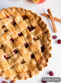 cranberry apple pie with lattice crust next to cinnamon sticks and fresh cranberries.