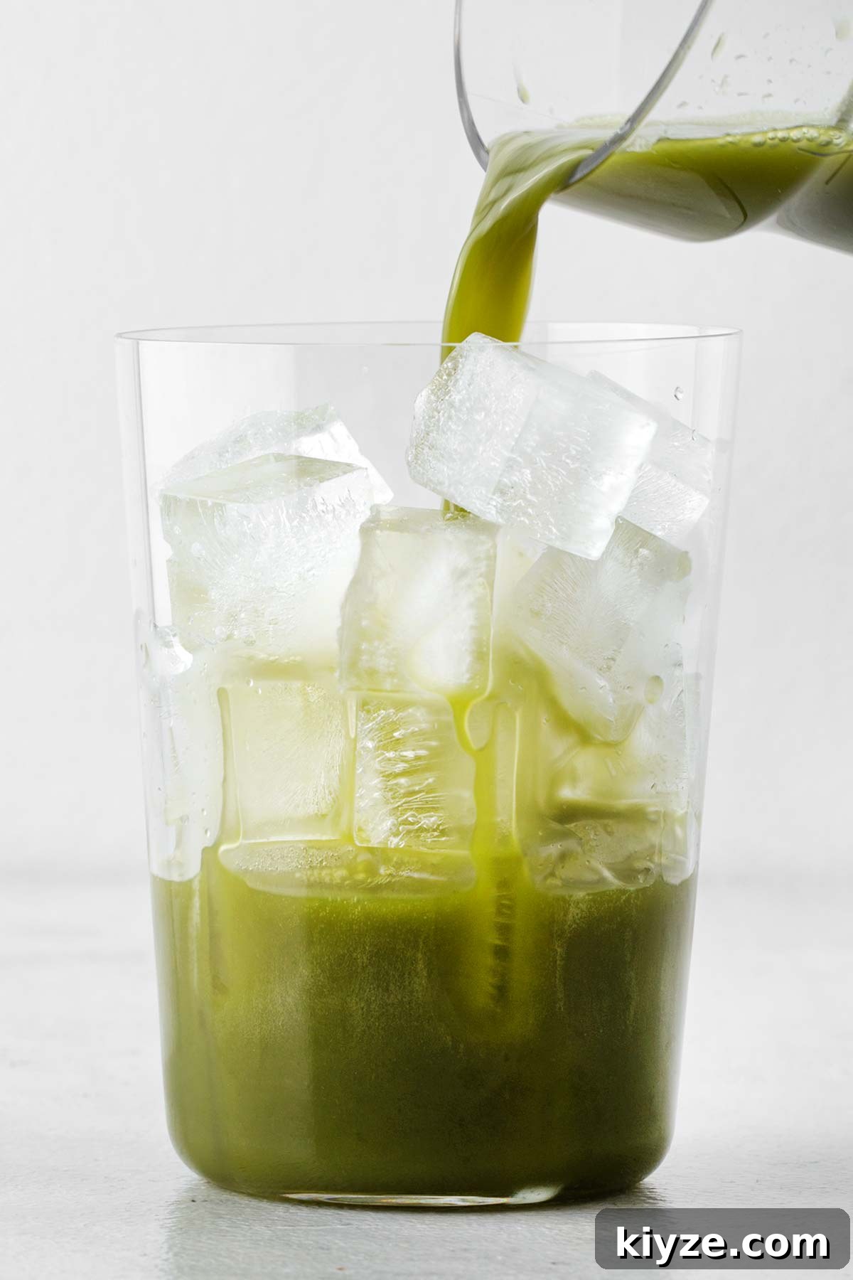 Iced Pineapple Matcha Latte Recipe: Refreshing Tropical Drink 8 Glass of ice with pineapple juice and matcha mixture being poured in.