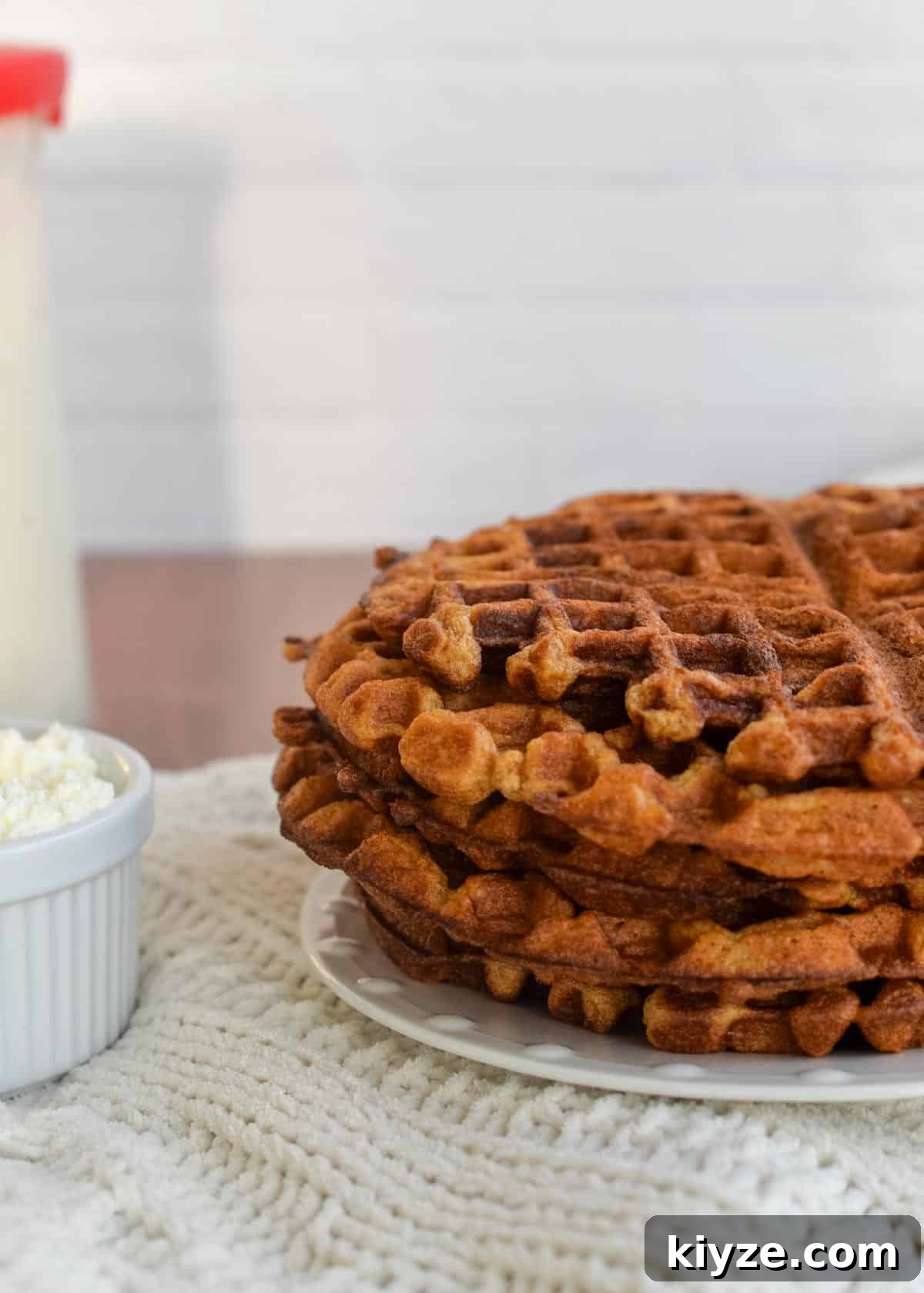Sourdough Gingerbread Waffles Recipe — Crisp Spiced Morning Treat 8 A stack of crispy gingerbread waffles on a plate with sourdough starter and bowl of whipped cream in the background.