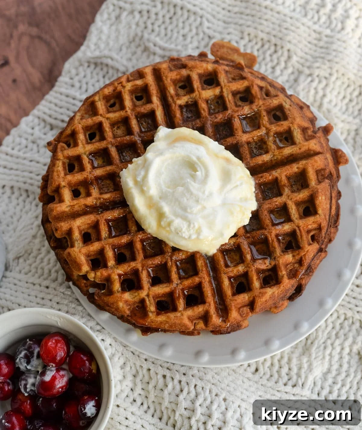 Sourdough Gingerbread Waffles Recipe — Crisp Spiced Morning Treat 9 A stack of gingerbread waffles on a plate with whipped cream in the center with a bowl of cranberries to the side.