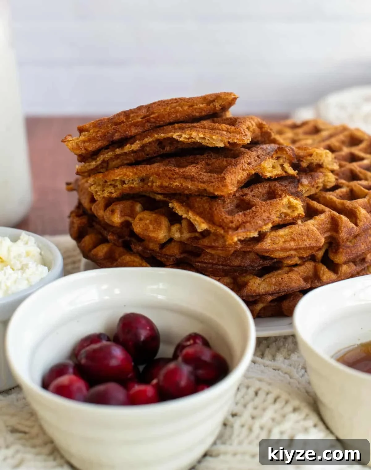 Sourdough Gingerbread Waffles Recipe — Crisp Spiced Morning Treat 10 A stack of sourdough gingerbread waffles on a plate with a bowl of cranberries in front of them.