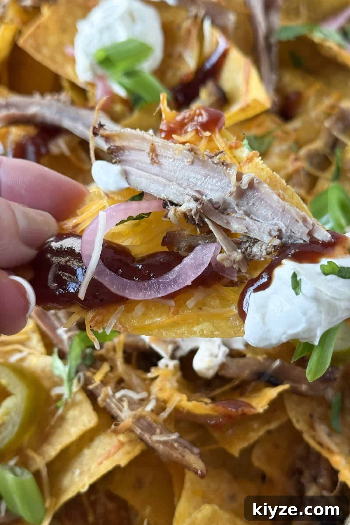 Graduation Party Menu Ideas: 6 Crowd-Pleasing Meal Plans 5 Hand holding a loaded BBQ pulled pork nacho with melted cheese, sour cream, and pickled red onions.